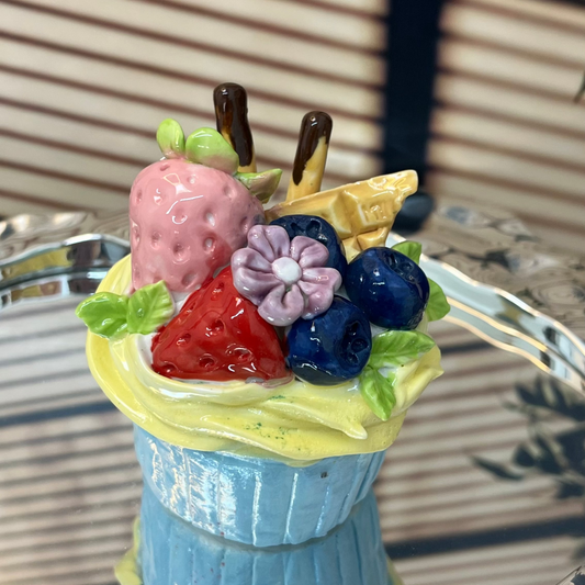Toy ice cream cone with fruit toppings on a reflective surface